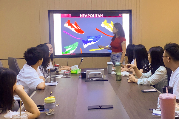 XINZIRAIN team members discuss product development in a meeting room, reviewing both mechanized production blueprints and handcrafted design samples, demonstrating integrated expertise across production methods.